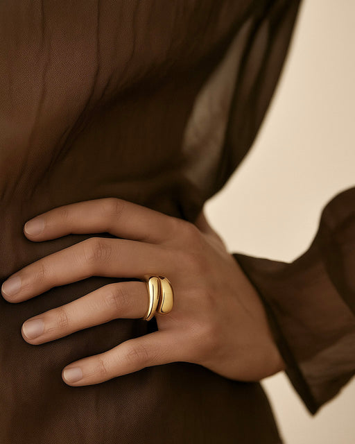 Close-up of a hand wearing sculptural gold ring over a sheer brown blouse, showcasing minimalist jewelry from Mirada Kollektive.