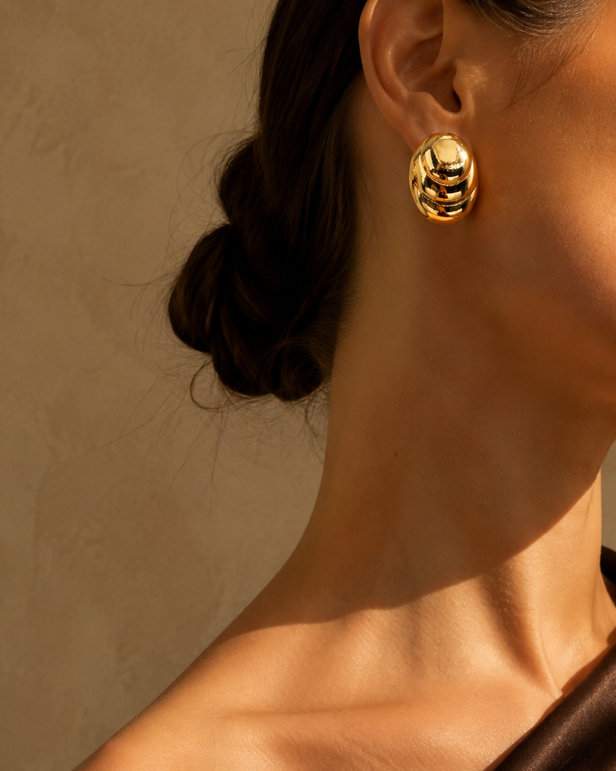 Close-up of a person wearing gold earrings against a neutral background
