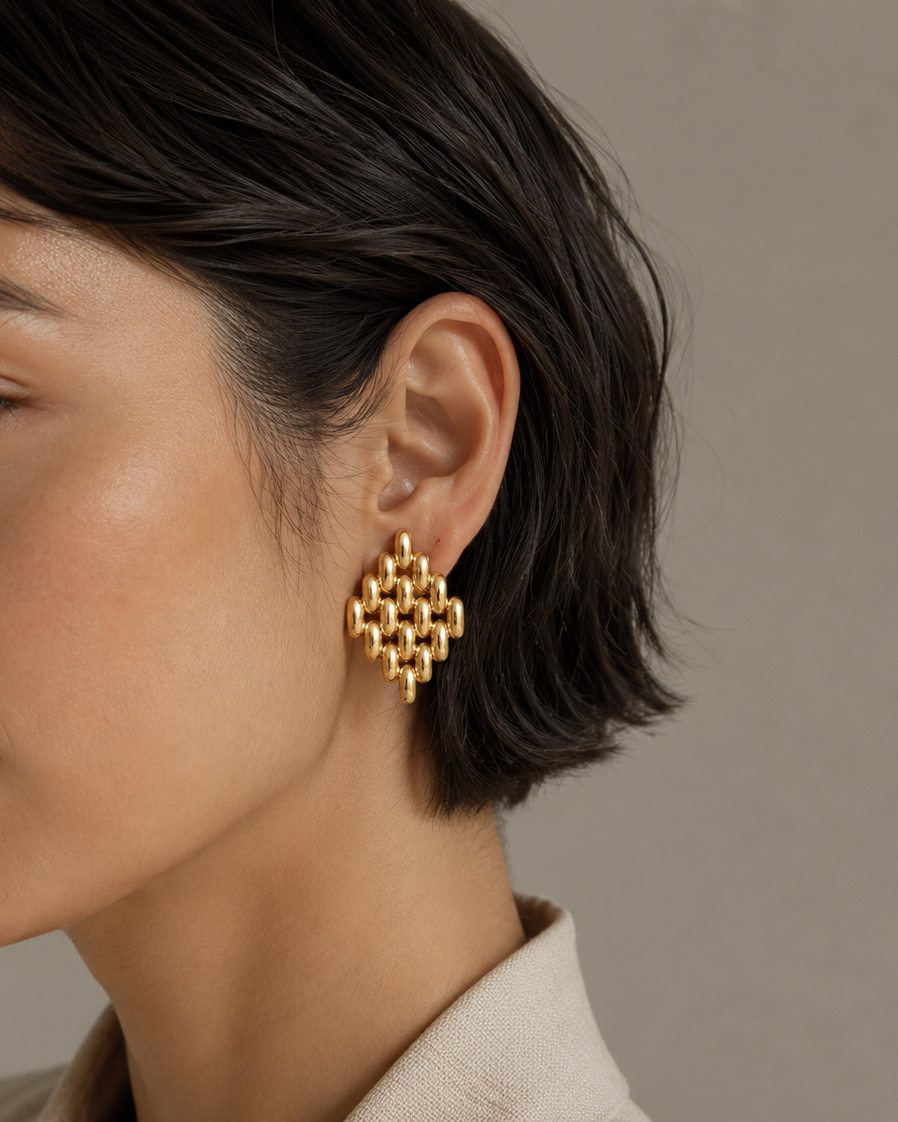 Close-up of a person wearing gold earrings with a neutral background