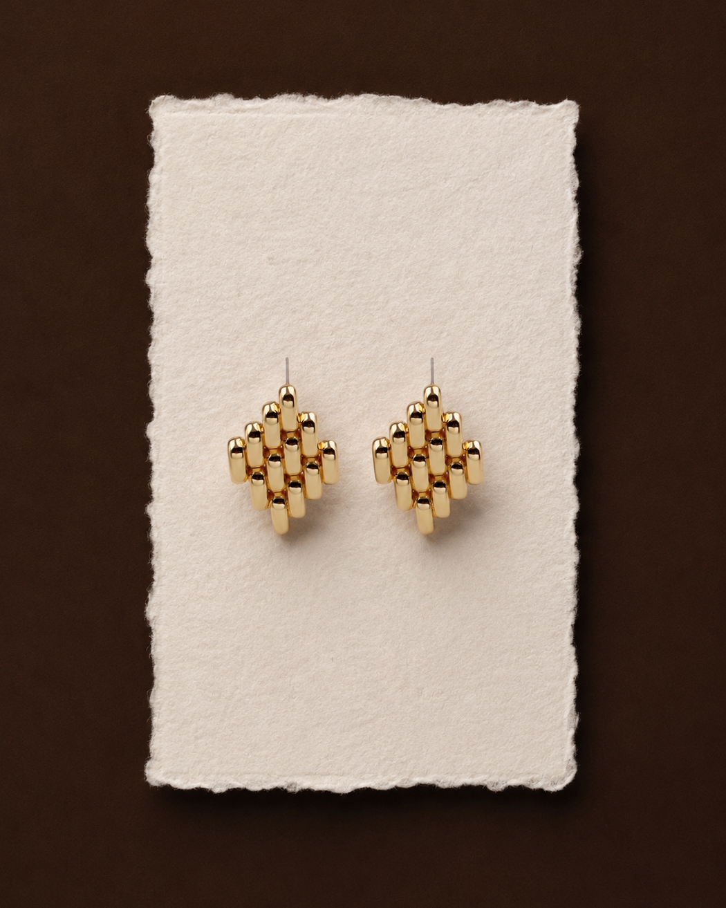 Gold geometric earrings on a white card with a brown background