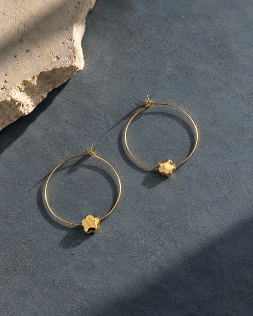 CHLOE gold floral hoop earrings with delicate flower charms on a textured slate blue background.