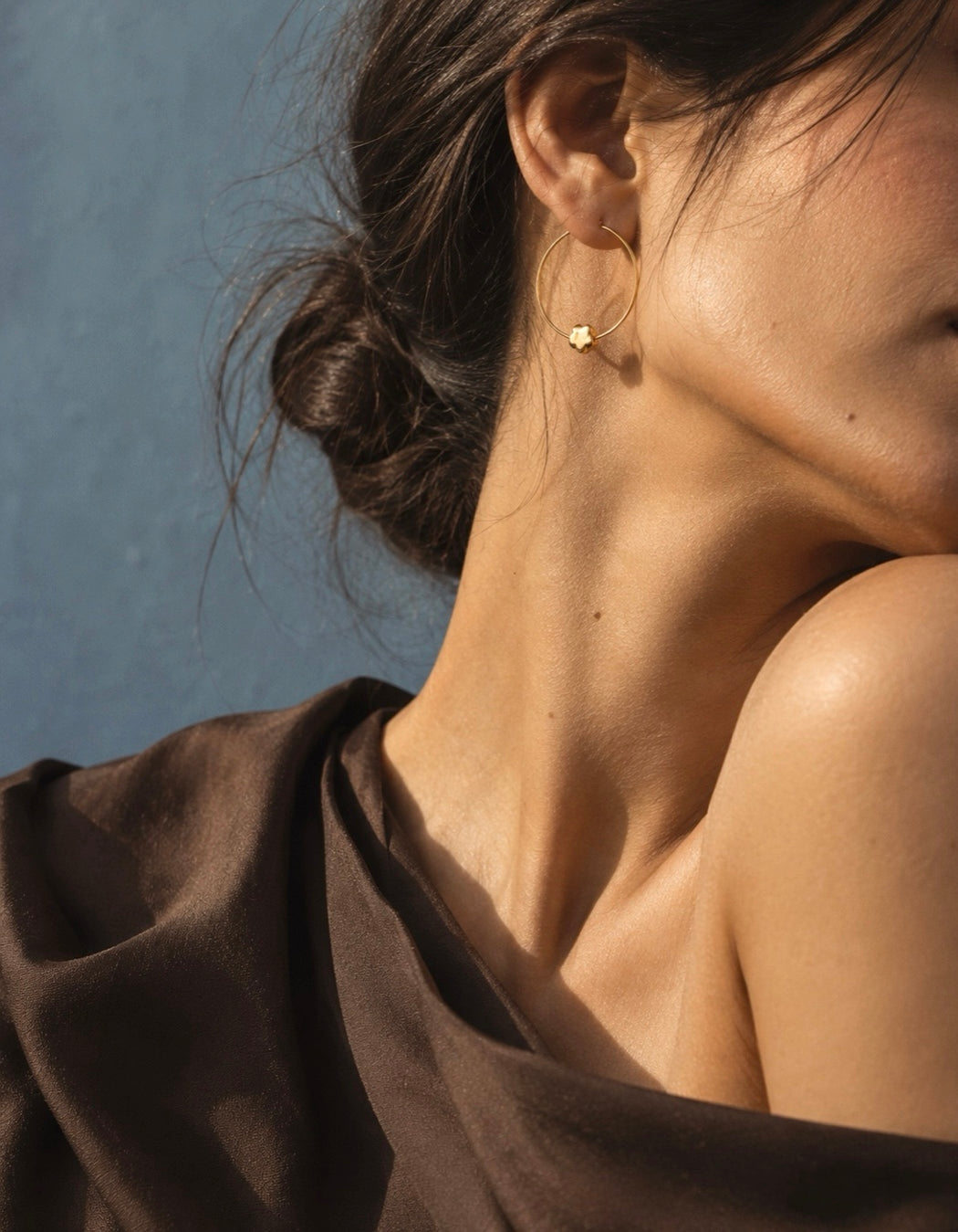 Close-up of CHLOE gold-tone hoop earrings featuring sculptural flower charms and slender hoops.