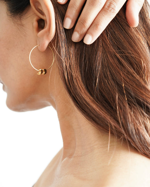 Model wearing Freya gold hoop earrings with long hair tucked behind ear