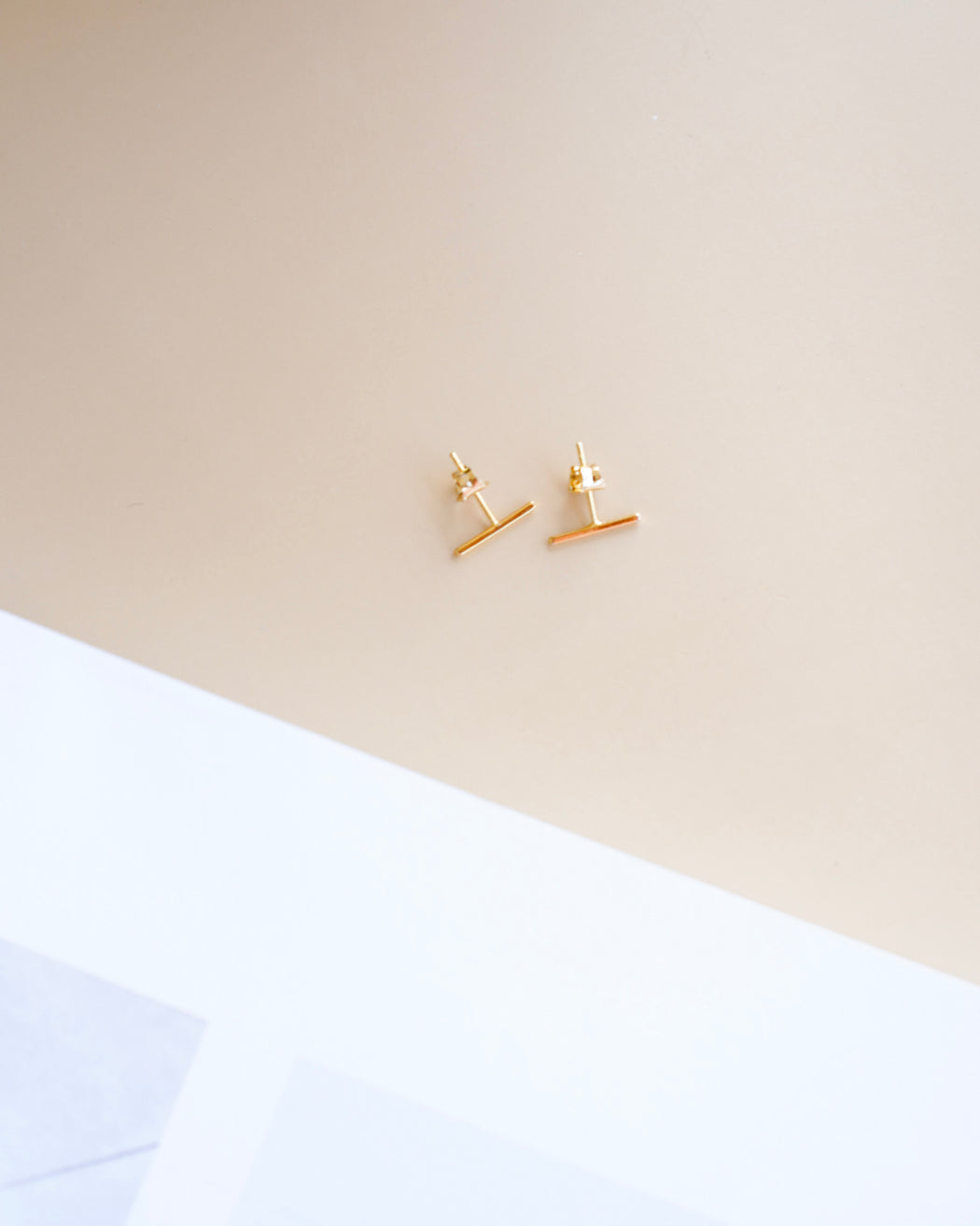 Pair of slim gold minimalist bar earrings on neutral background, Sloan studs by Mirada Kollektive.